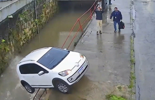Carro sem motorista atravessa rua e cai em rio em Petrópolis; vídeo mostra reação de homem que leva as mãos à cabeça ao ver a situação
